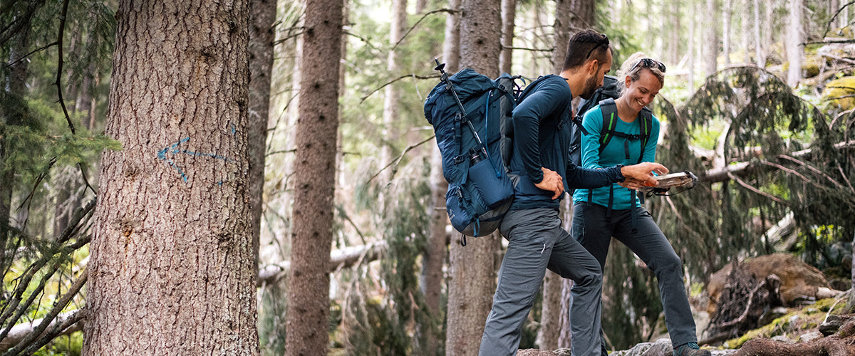 A man and woman hiking in the woods with backpacks on looking at their map