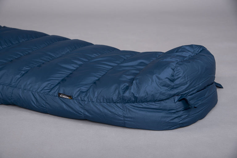 The foot end of a Pipedream 400 lightweight 3 season sleeping bag in blue laid on the floor on a grey background